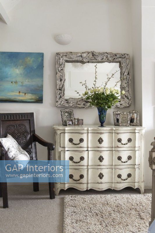 Ornate chest of drawers and carved monks chair in country bedroom