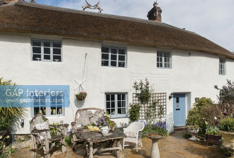 Exterior of thatched country cottage with rustic garden furniture