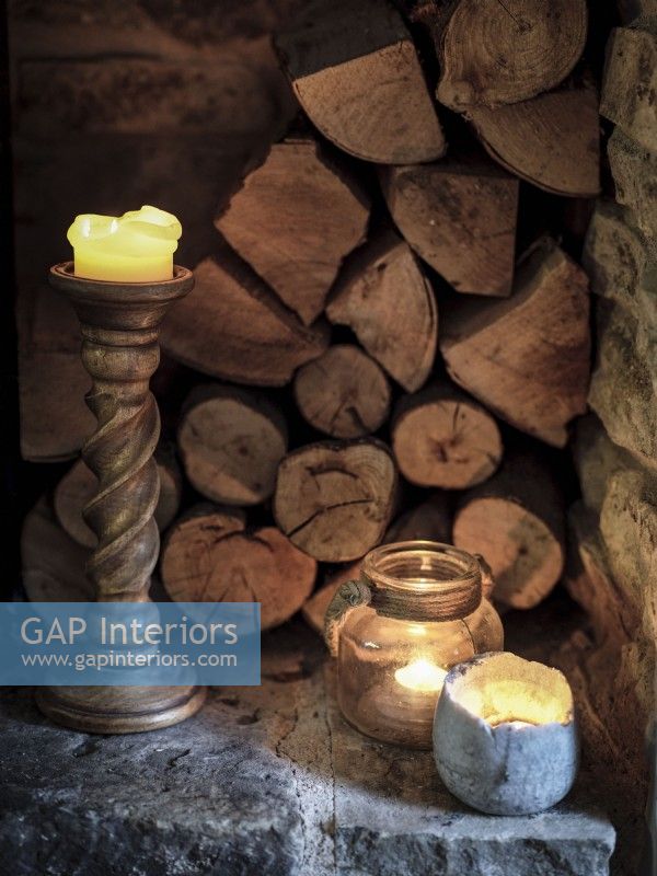 Candles and stacked logs beside chimney breast