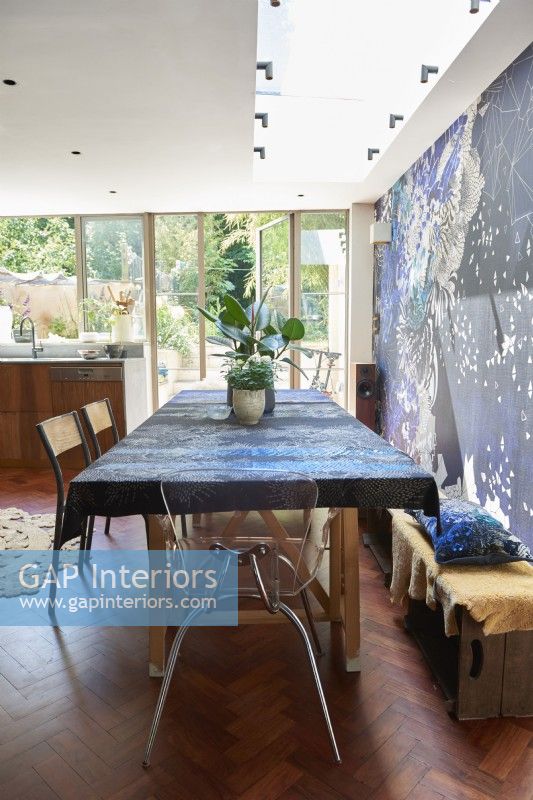 A dining table with a designer blue patterned table cloth next to a designer wallpaper feature wall.