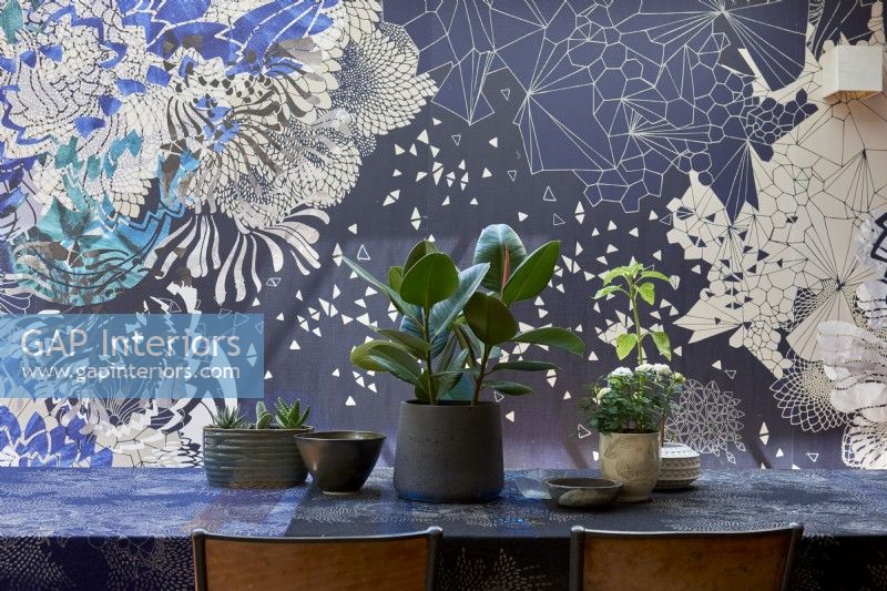 Detail of a dining table with plants and designer wallpaper .