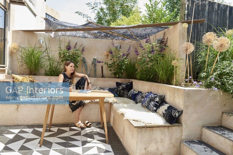 Owner sitting at her table and built in concrete bench in her garden .