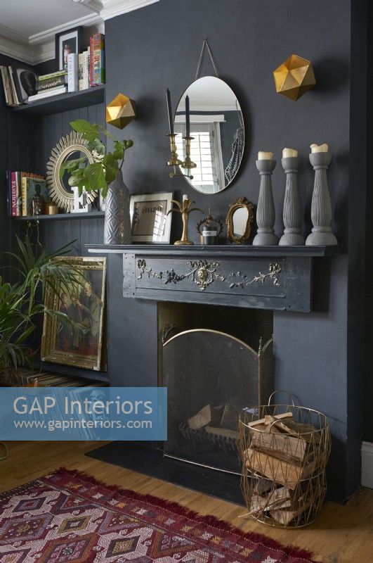 A fireplace on a dark grey wall with a collection of ornament on the mantlepiece. 