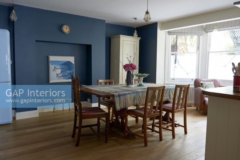 Retro dining table and chairs in a dark blue painted room .