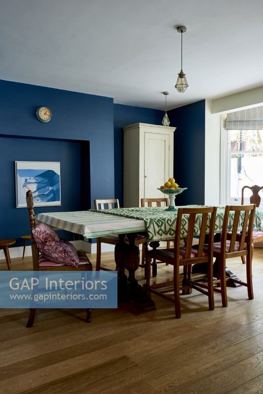 Dining room with dark blue painted walls, and vintage, antique table and chairs. 
