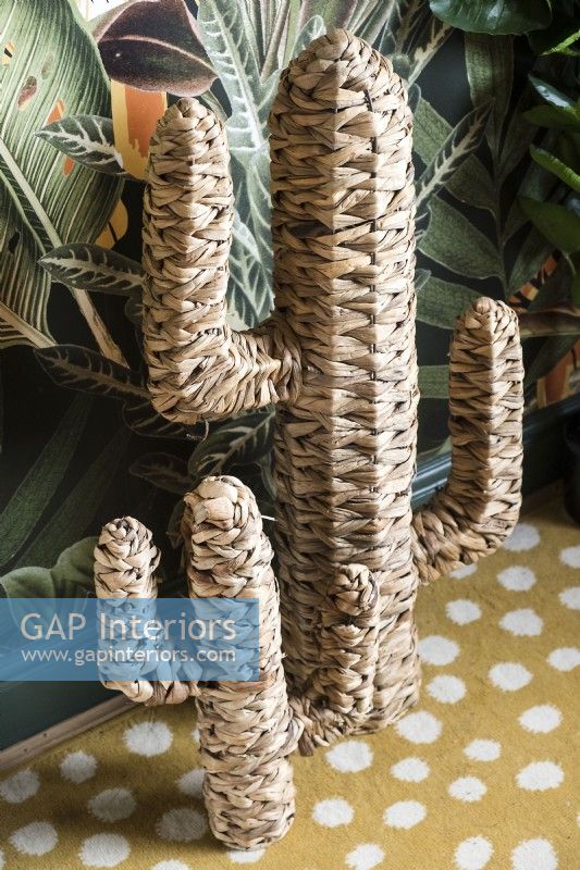 Straw woven cactus ornament against tropical patterned wallpaper