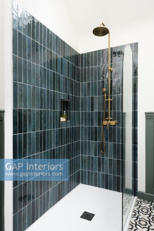 Green tiled shower unit in a bathroom with brass shower fixtures