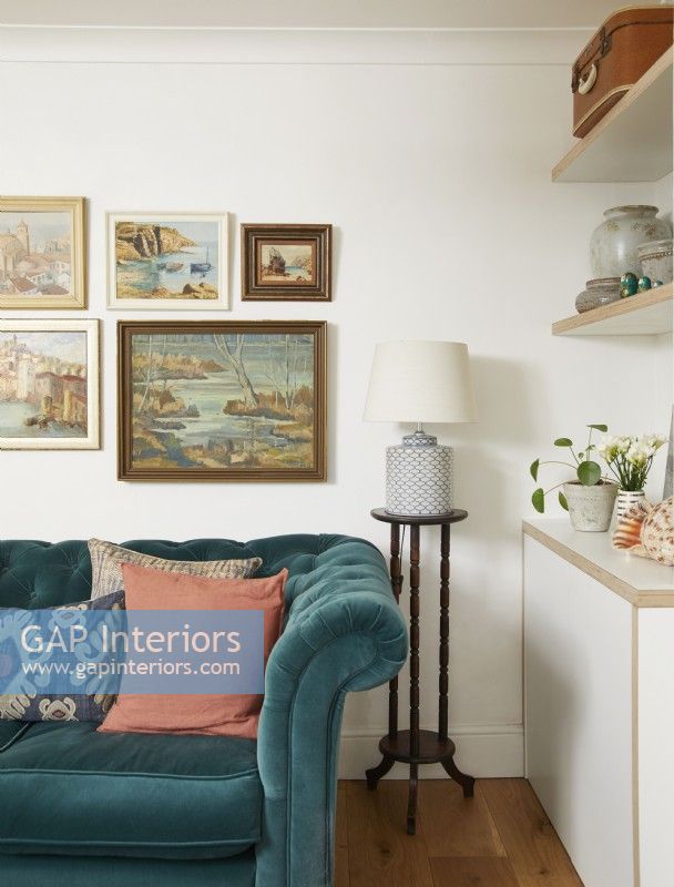 Living room detail with a teal blue sofa, vintage oil paintings on the wall and lamp.