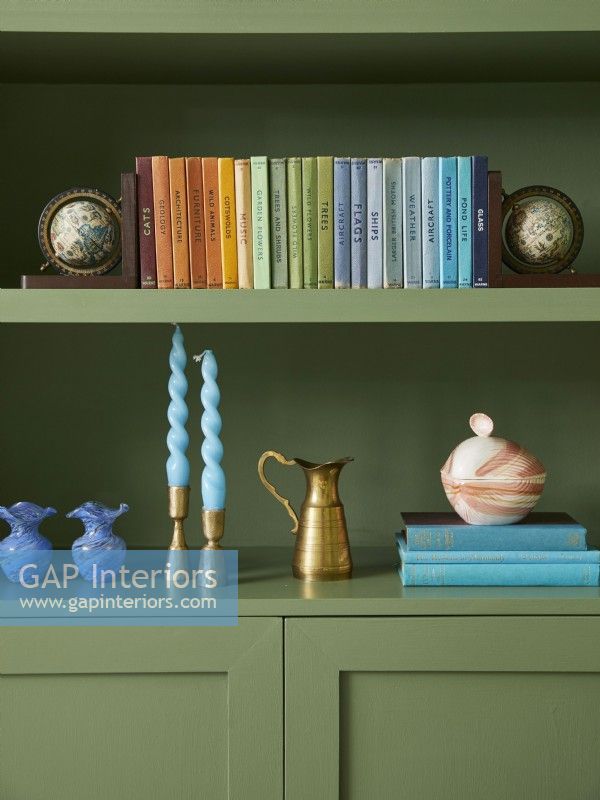 Living room detail with green painted shelving with rainbow collection of books and ornaments.