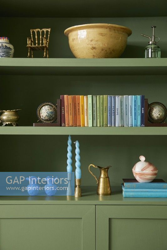 Living room detail with green painted shelving with rainbow collection of books and ornaments.