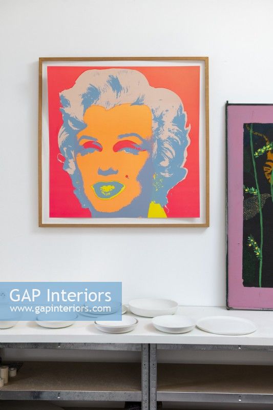 Colourful painting of Marilyn Munroe above table of white ceramics