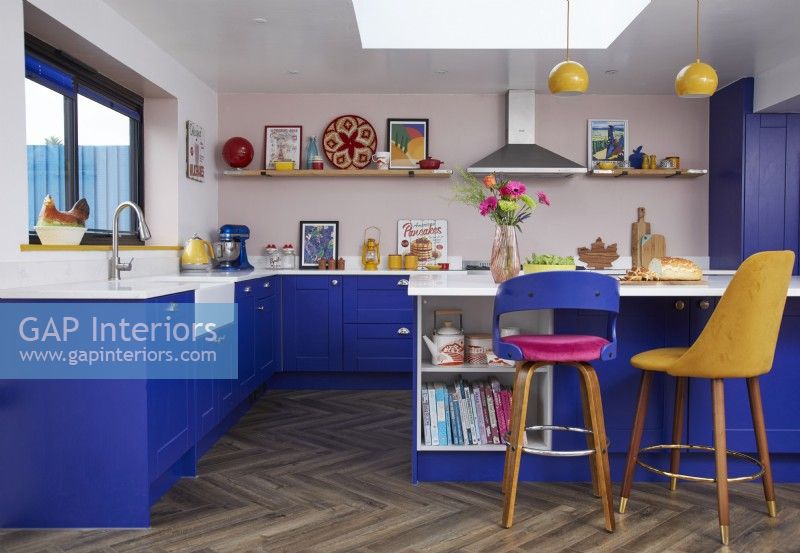 Colourful kitchen with cobalt blue cabinets, a breakfast bar and wooden flooring.