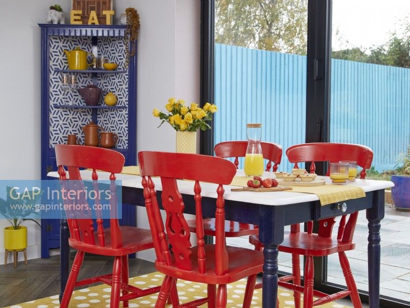 Open-plan dining area detail with red painted chairs and a yellow spotty rug.
