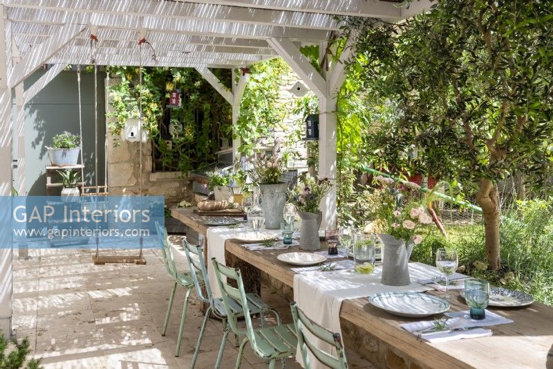 Swing hanging from pergola on rustic terrace with dining area
