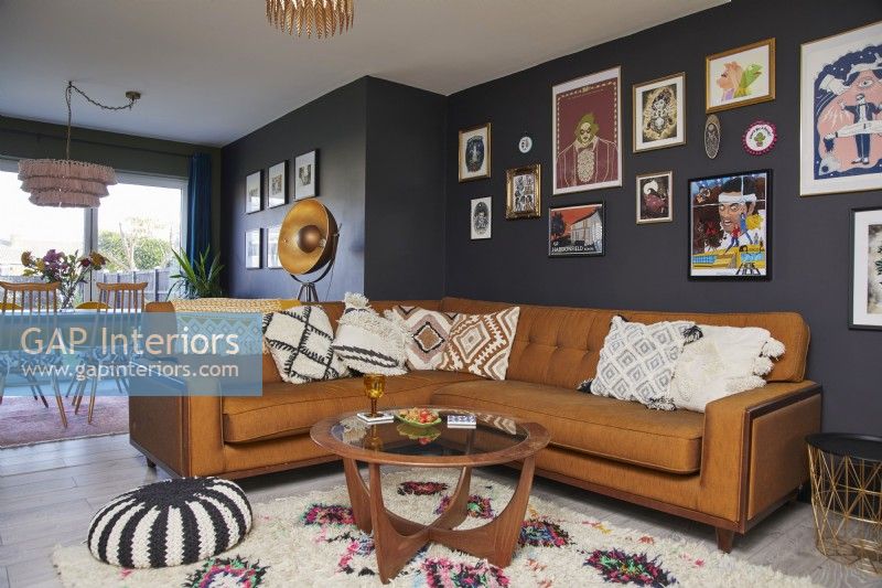 Living room with a brown leather sofa, vintage coffee table, a gallery of framed prints and dark blue painted walls.