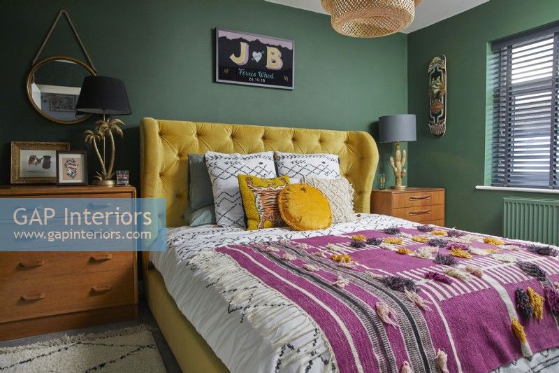 Bedroom with yellow double bed, wooden vintage drawers and green painted walls.
