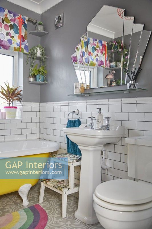 Colourful bathroom with a yellow freestanding bath, white metro tiles and a fan shaped mirror.