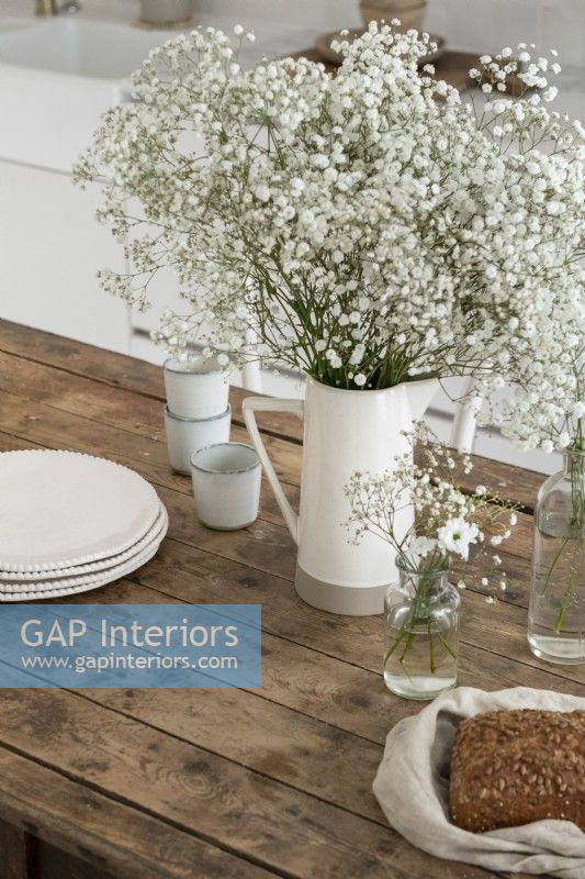 White flowers and jug on wooden country kitchen table