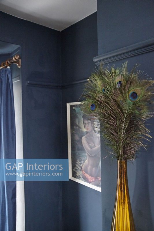 Living room detail showing decorative peacock feathers in a vase, retro artwork and navy blue painted walls.