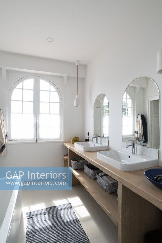 Arched mirrors over twin sinks in bathroom with arched windows
