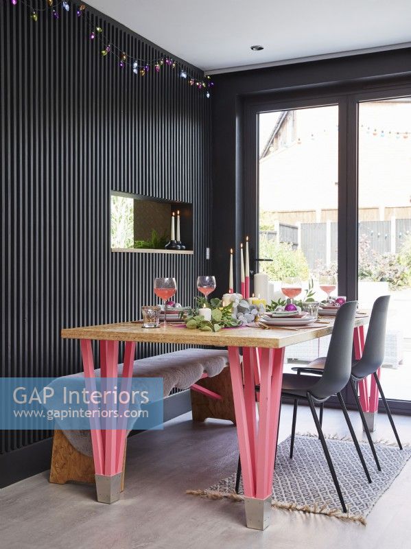 Open plan dining room with black panelling. OSB dining table with pink neon legs and a Christmas table setting.