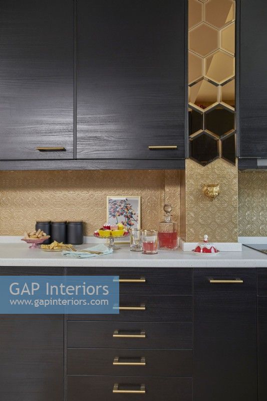 Kitchen detail showing dark brown cabinets, gold mirror tiles and gold painted textured wallpaper.