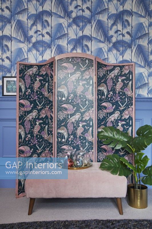 Living room detail showing a patterned screen, jungle print wallpaper and blue panelling.
