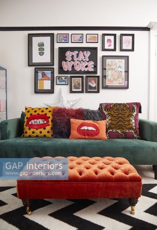 Colourful living room with green sofa, orange footstool and a gallery wall.
