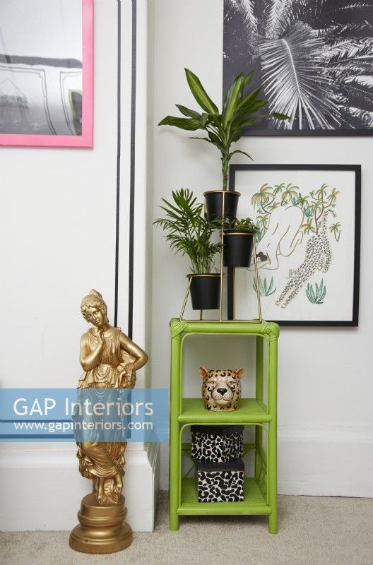 Bedroom detail with a black faux panelling effect (using black washi tape), framed artwork, green shelving with plants and a gold statue.