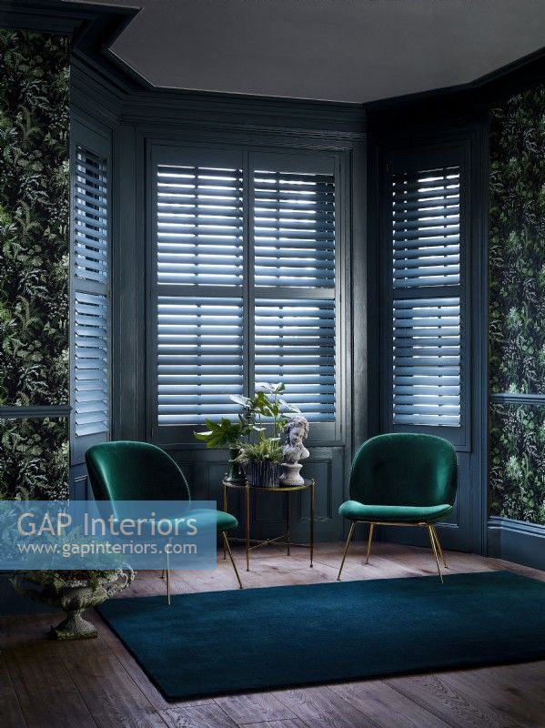 Living room with green chairs, patterned wallpaper and shutters