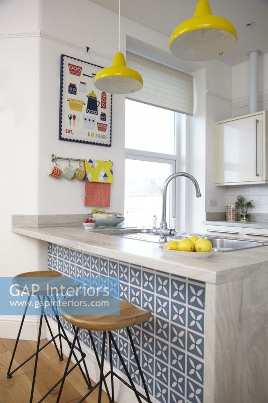 Breakfast bar in an open plan kitchen-diner. With blue vinyl tiles and yellow pendant lights.