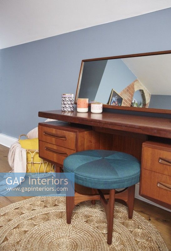 Bedroom detail showing a mid-century dressing table, teal stool and blue painted walls.