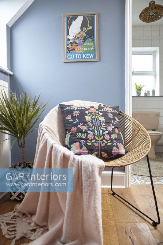 Bedroom detail showing a wicker chair, artwork on blue painted walls.