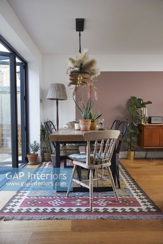 Dining area in an open plan living space with pink colour blocking and vintage furniture.
