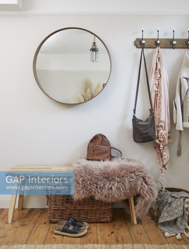 Entrance detail with coat hooks, a round mirror, a bench, and a wicker storage box.