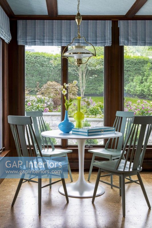 Round white pedestal dining table with wooden chairs and garden view.