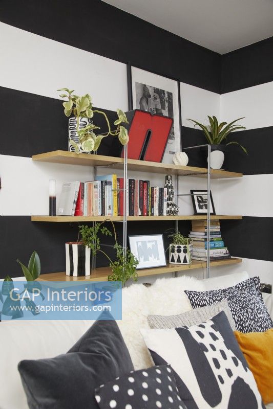Detail of open bookshelves in a modern open plan living room space with black and white striped walls. With hand painted concrete plant pots.
