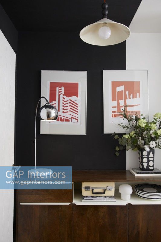 Hallway showing a retro sideboard with hanging graphic artwork above and black and white painted walls.