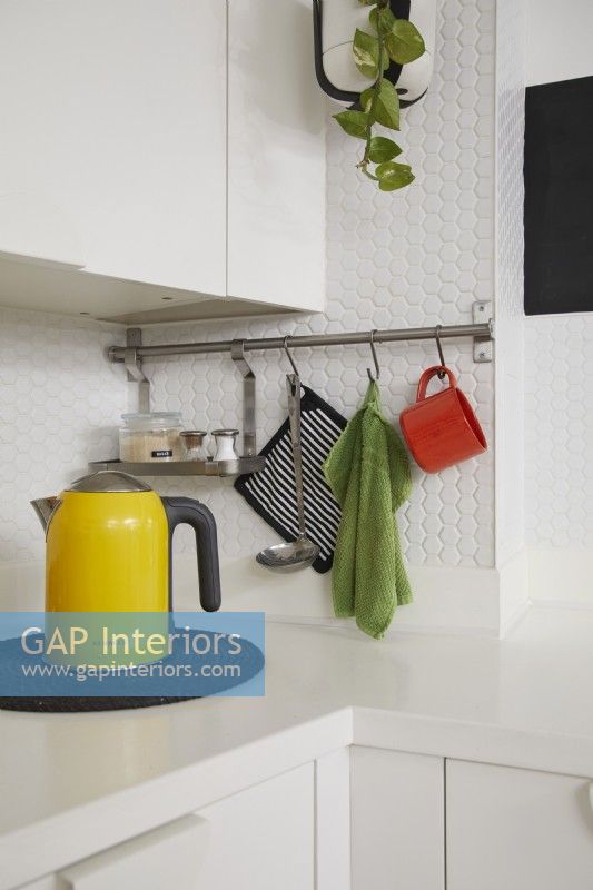 Contemporary kitchen detail showing yellow kettle, hanging utensils and white hexagon tiles.