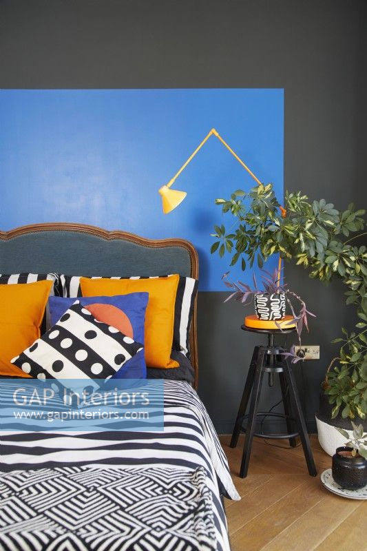 Bold and colourful painted bauhaus shapes in a contemporary bedroom. With an antique headboard, patterned soft furnishing and a yellow anglepoise lamp.
