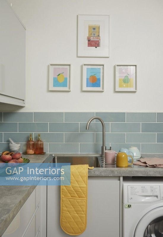 Kitchen with blue metro tiles showing the sink, artwork and crockery.