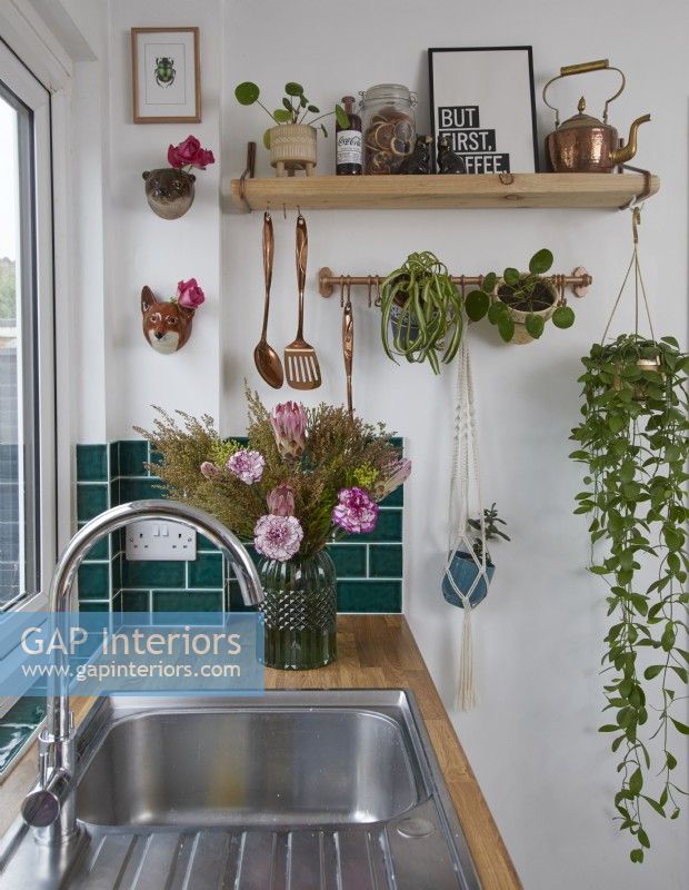 Detail of contemporary kitchen with sink, green metro tiles and open shelving with plants.