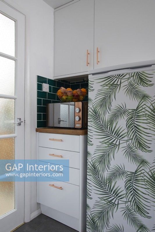 Kitchen detail showing fridge covered in jungle vinyl, microwave and a fruit basket.