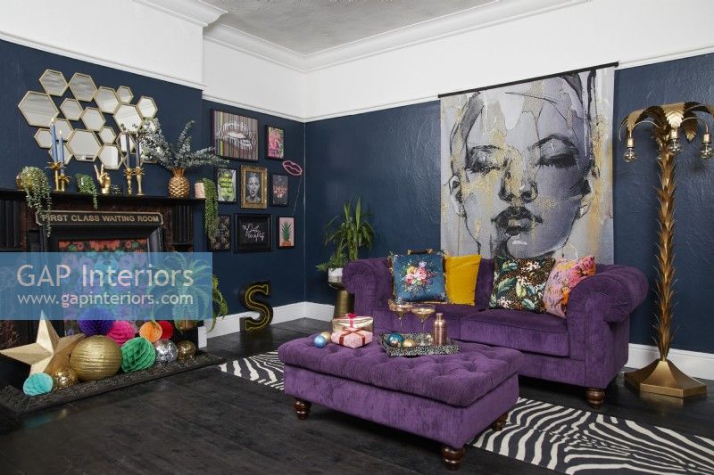 Living room with dark blue walls, a purple sofa and a fireplace with Christmas decorations.