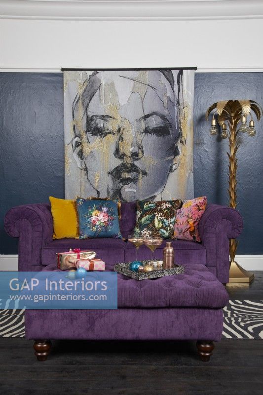 Living room with dark blue walls, a purple sofa and large illustrated poster of a woman.