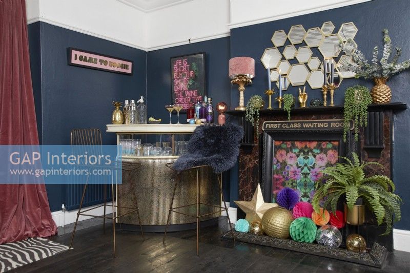 Living room with a gold drinks bar, dark blue painted walls and a decorated fireplace.