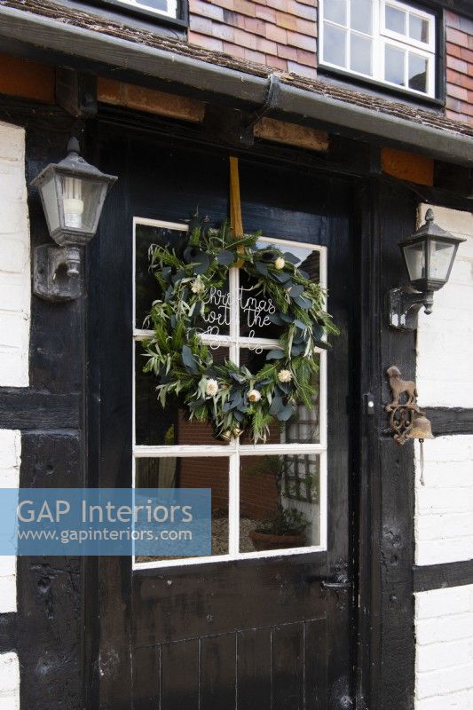 Christmas wreath on a black and white country cottage front door with vintage outdoor wall lights