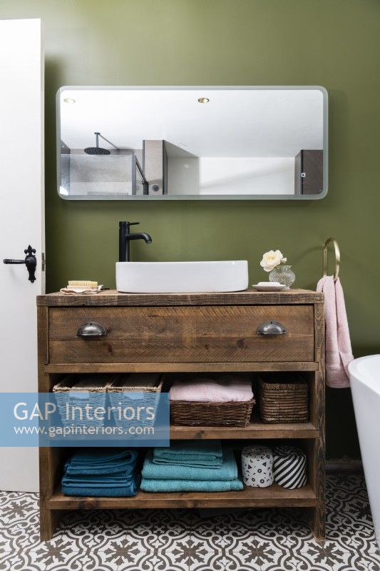 Bespoke handmade wooden vanity unit with white bathroom sink against a green wall