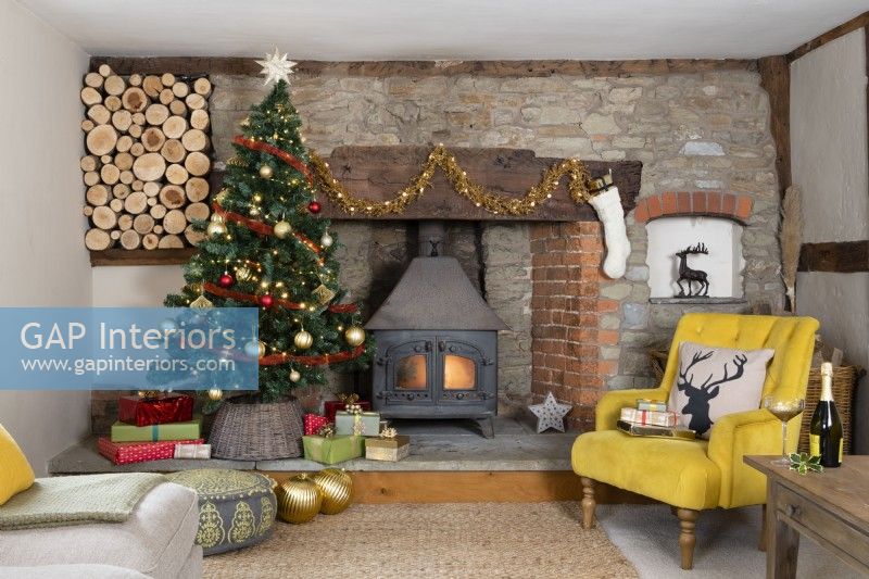 Country house living room with Christmas tree and wood burning stove and log store in a stone and brick inglenook fireplace 
