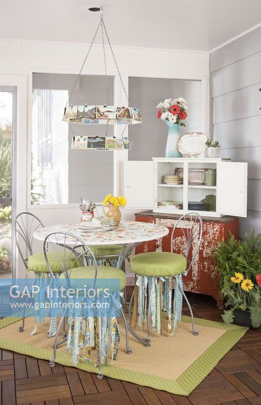 Dining area of 3-season porch with painted table, vintage postcard chandelier and cabinet storage